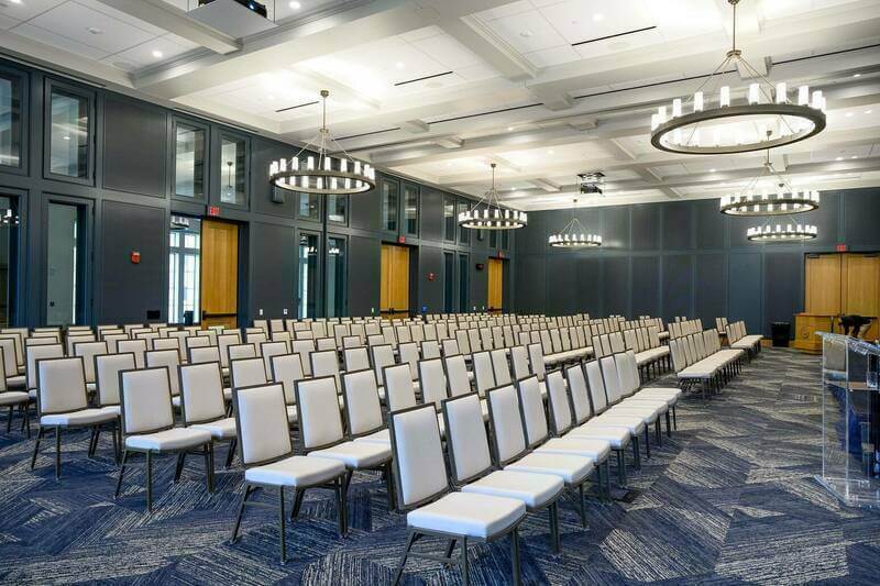 Dark grey walls surround white chairs as circular chandeliers hang from the ceiling and provide lighting in McKenna Hall conference room